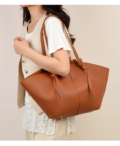 Brown lychee leather tote bag featuring a trapezoidal silhouette and knot strap detail