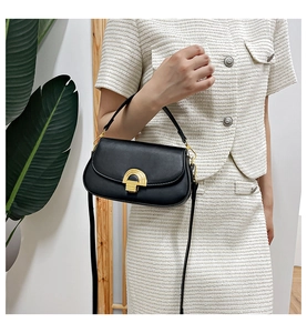 Détail du sac selle vintage en cuir noir avec fermoir doré sur une tenue en tweed