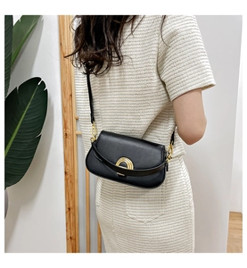 Détail d'un sac besace en cuir noir avec fermoir doré porté sur une robe en maille blanche