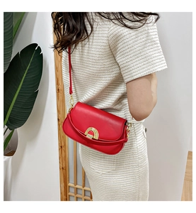 Détail du sac selle en cuir mat rouge avec boucle en métal doré porté par un mannequin