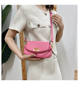 Gros plan d'un sac selle en cuir rose avec boucle dorée sur une tenue en tweed blanc cassé