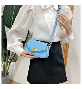Détail d'un sac besace bleu clair avec boucle dorée porté par un mannequin en tenue chic
