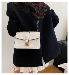 Detail of white crocodile pattern chain bag with golden butterfly lock on a shoulder
