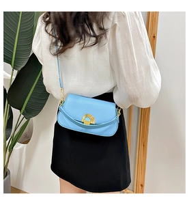 Vue détaillée d'un sac selle bleu clair avec boucle en métal doré porté par un mannequin