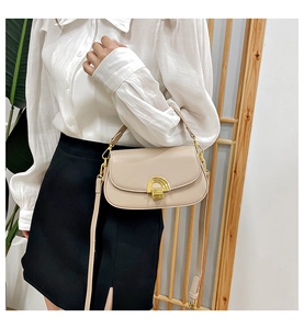 Gros plan du sac bandoulière beige avec boucle dorée porté par un mannequin en décor