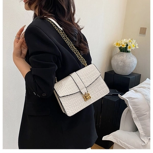 Detail of white crocodile pattern shoulder bag with gold chain and metal buckle on a model