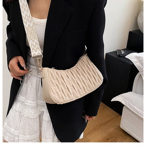 Détail du sac plissé crème avec une large bandoulière tissée à motifs et boucles dorées