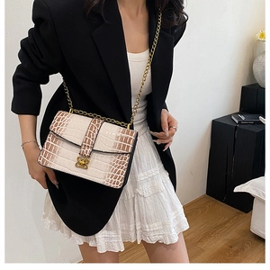 Detail of crocodile pattern crossbody bag with gold clover lock and chain on model
