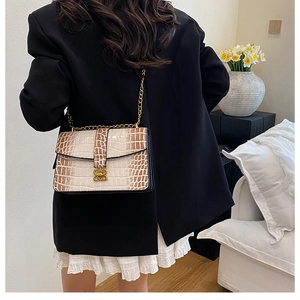 Detail of crocodile embossed crossbody bag with golden bow lock and chain strap