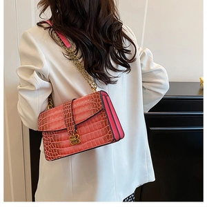 Detail of coral pink crocodile embossed bag with gold B-shaped buckle and chain strap