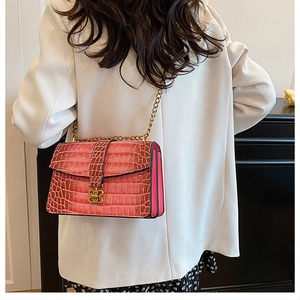 Detail of fuchsia crocodile pattern chain bag with golden B-shaped buckle on white blazer