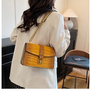 Detail of yellow crocodile embossed crossbody bag with golden chain and clasp in elegant interior