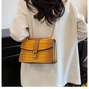 Detail of yellow crocodile embossed crossbody bag with gold chain and butterfly lock
