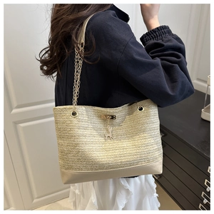 Detail view of woven straw tote bag with gold chain strap and deer charm on a model