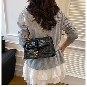 Close-up of black crocodile pattern crossbody bag with gold butterfly clasp worn by a model