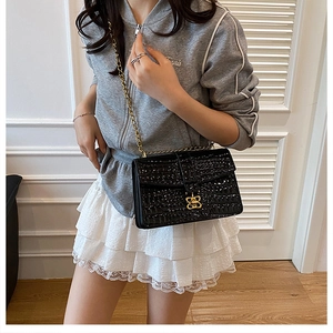 Detail of black crocodile texture bag with gold chain strap and butterfly metal clasp