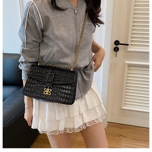 Detail of black crocodile texture bag with gold bow clasp and metallic chain strap