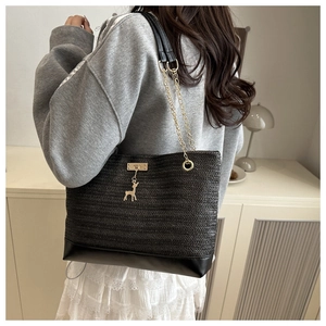 Detail of black straw tote bag with gold deer charm and chain shoulder strap