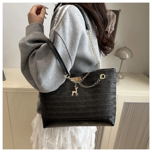 Close-up of black woven tote bag featuring gold reindeer pendant and metal chain strap
