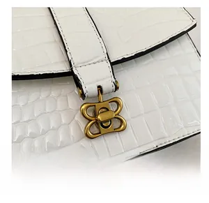 Detail of golden metal twist lock and white crocodile embossed leather handbag