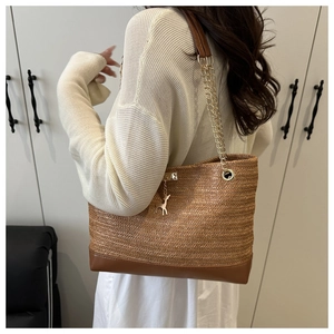 Detailed view of brown woven tote bag featuring gold chain strap and metal deer pendant