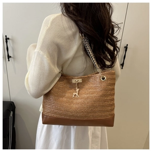 Detail of straw woven tote bag featuring gold chain strap and deer charm on brown texture