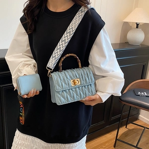 Quilted light blue handbag with bamboo handle and patterned strap shown in modern setting