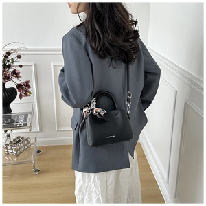 Detail of black pebbled leather bucket bag with decorative silk scarf and metal hardware
