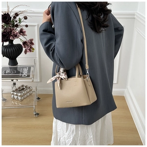 Close-up of beige lychee grain leather bucket bag with decorative printed silk scarf handle