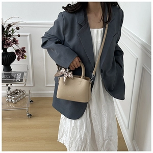 Detail of beige lychee pattern leather bucket bag with decorative scarf handle decoration