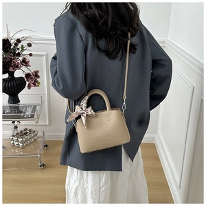 Detail of beige lychee texture leather handbag with pink silk scarf and metal strap