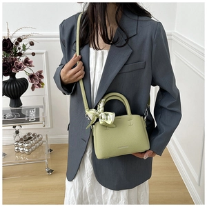 Detail of avocado green leather bucket bag with silk scarf on handle and fine texture