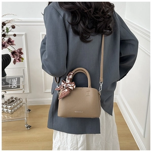 Close-up of khaki litchi grain leather bucket bag with decorative printed silk scarf