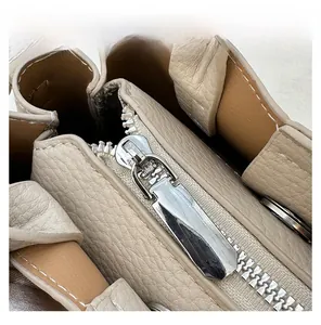 Detail view of smooth metal zipper puller and pebbled leather texture on beige handbag