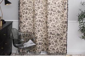 Close-up of floral linen curtain with black tassel fringe and vintage botanical pattern