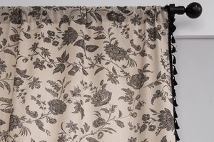 Detail of bohemian linen curtain with black floral print and decorative pom-pom tassels