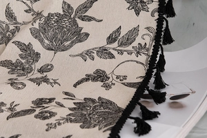 Detail of vintage floral print fabric with black fringe tassels on linen textured curtain