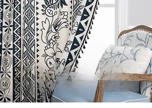 Detail of blue and white ethnic floral curtains with black pom-pom tassel trim accents