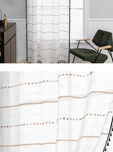Detail of white semi-sheer curtain featuring colorful pompom stripes and black tassel trim