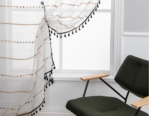Detail of white sheer curtain with multi-color stripes and black tassel fringe trim
