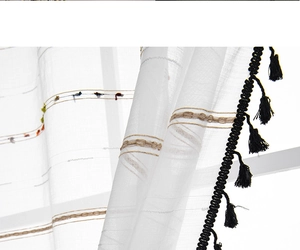 Detailed view of white sheer curtain featuring black fringe tassels and colorful embroidery