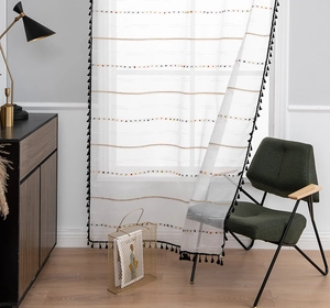 Detail of white semi-transparent curtain with chic black tassels and colorful embroidery