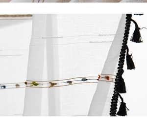 Close-up of white semi-sheer fabric with colorful embroidery and black tassel edge