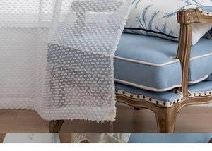 Dettaglio della tenda voile bianca semitrasparente con pom-pom Swiss dot e filtro luce
