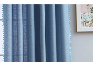 Detail eines blauen Vorhangs mit Leinentextur und dekorativer Pompon-Borte an den Rändern