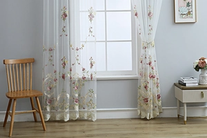 Detail of floral embroidery on semi-sheer white curtains with pink roses and lace edges