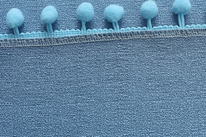 Makrodetail aus blauem strukturiertem Stoff mit hellblauen Pompons und Ziernaht
