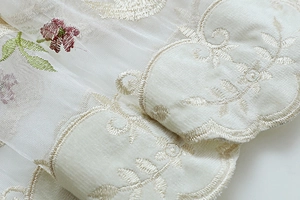 Macro detail of embroidered sheer curtain fabric with floral patterns and scalloped edges