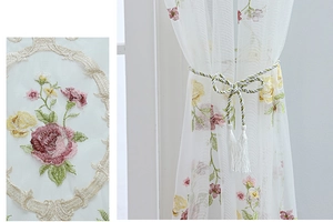 Detail of floral embroidery on white semi-sheer curtain with woven tassel tieback