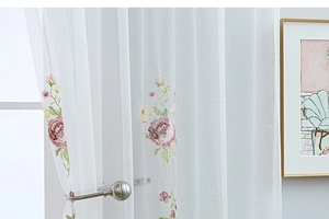 Detail of white semi-sheer tulle curtain with delicate pink floral embroidery and green leaves